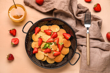 Composition with frying pan of mini pancakes, strawberry and bowl of honey on color background