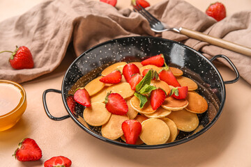 Frying pan with tasty mini pancakes and strawberry on color background