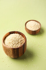 Wooden bowls with sesame seeds on green background