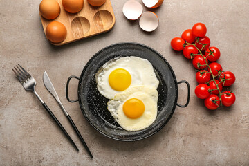 Frying pan with tasty eggs, tomatoes and cutlery on grunge background