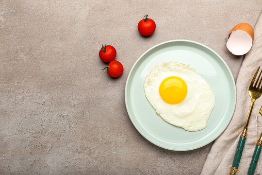 Plate with tasty fried egg and tomatoes on grunge background