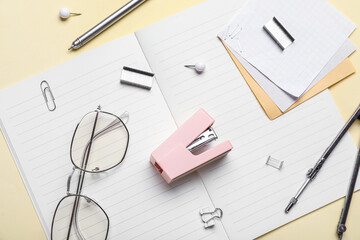 Stapler with different stationery supplies and eyeglasses on yellow background