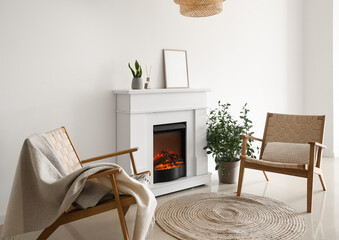 Modern fireplace with blank frame, houseplants and armchairs near light wall