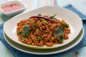 Spicy duck pad kra pao or pad kra pao ped, minced duck stir-fried with holy basil leaves, ground dried chilis and chopped garlic cloves to create this savory Thai dish, served on a beige-white plate.