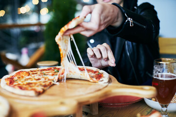 A woman takes a slice of pizza at a pizza parlor. Pulling cheese, yummy pizza. Front view.
