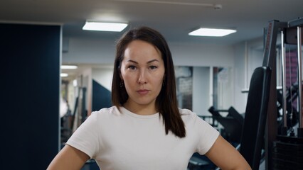 Fototapeta na wymiar Portrait of a young woman of oriental appearance in the gym. A woman with a slight smile looks into the frame. Gym personal trainer looking at the camera. The concept of exercising in the gym.