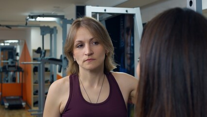 Two women in the gym are talking about the training process for burning fat. A personal trainer tells you how to eat and exercise to lose weight. Trainer woman in the gym leads a lecture.