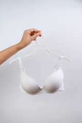 A young woman is holding a hanger with a bra. Closeup. Front view.