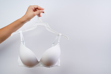 A young woman is holding a hanger with a bra. Closeup. Front view.