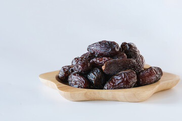 Medjool dates in a wooden plate on a white background. It is a wonderful fruit and has a variety of benefits.