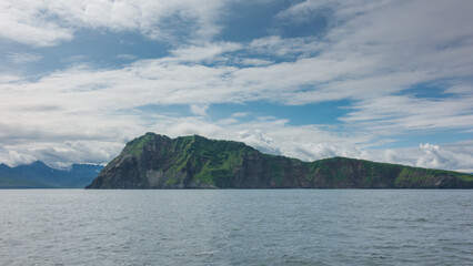 The picturesque rocky coast of Kamchatka against the background of blue sky and clouds. Ripples on the surface of the Pacific Ocean. Avacha Bay