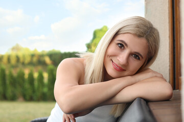 Portrait of beautiful woman sitting near house in yard, space for text