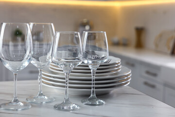 Clean glasses, dishware and cutlery on white marble table in kitchen