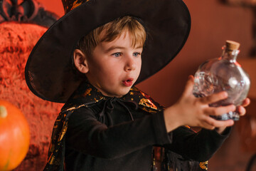 Fototapeta premium Little cute boy in a black magician.costume and hat in Halloween decorations.Halloween concept.Selective focus.