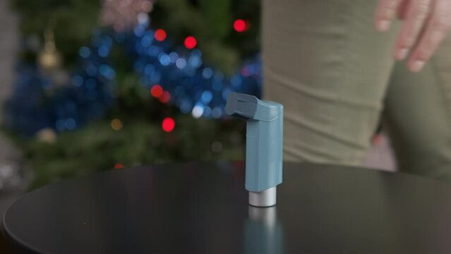 Allegry problems at new year. A woman hand puts an inhaler on the table by the decorated tree. A concept of allergy problems at New Year party.