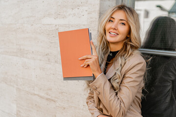  Close up photo of Elegant sucsessful blond  woman in stylish casual outfit posing   on the street. Holding advertising catalogs.