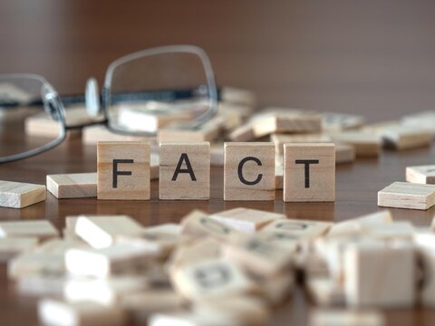 fact word or concept represented by wooden letter tiles on a wooden table with glasses and a book