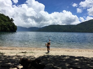 夏の湖で水着で長い枝を持って遊ぶ帽子をかぶった男の子
