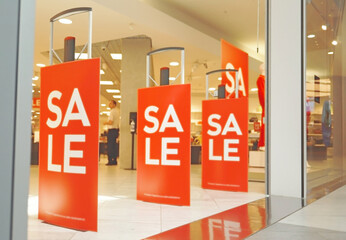 Blurred image of Sale signs at the entrance to a clothing store. Large red panels with white words. Sale in a mall. Seasonal discount offer in store. Discounts and Black Friday concept. Shopping sale