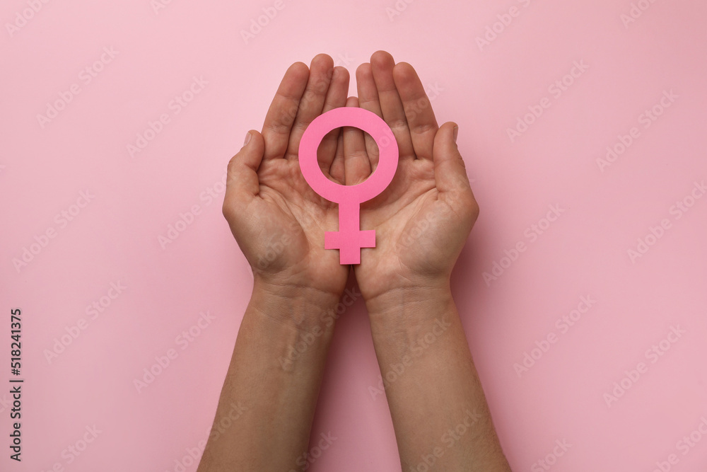 Wall mural woman holding female gender sign on pink background, top view