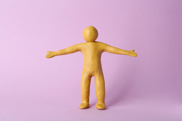Human figure with arms wide open made of yellow plasticine on violet background