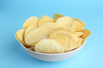 Bowl of tasty potato chips on light blue background