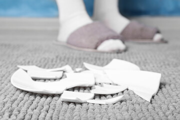 Woman in slippers standing near broken plate on rug at home, closeup