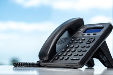 telephone with VOIP on white table by window with blurred sky background. customer service support,...