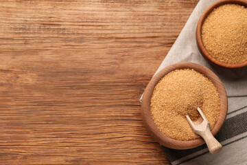 Brown sugar in bowls on wooden table, flat lay. Space for text