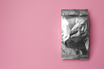 Blank foil package on pink background, top view. Space for text