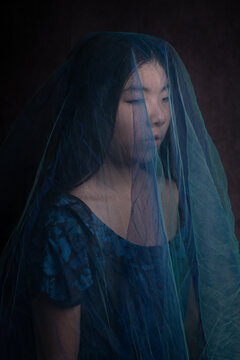classic studo portrait of asian woman in a dress hiding under blue veil