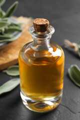 Bottle of essential sage oil and leaves on black table