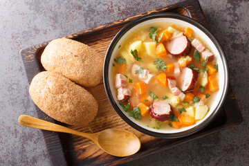 Portion of hot pea soup with potatoes, onions, carrots, bacon and sausages close-up in a bowl on the table. Horizontal top view from above