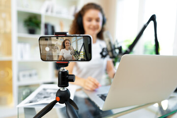 Young curly female blogger recording video at table at home