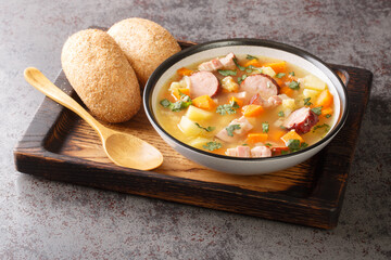 Portion of hot pea soup with potatoes, onions, carrots, bacon and sausages close-up in a bowl on the table. Horizontal
