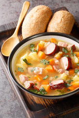 Delicious pea soup with vegetables, bacon and sausages close-up in a bowl on the table. Vertical