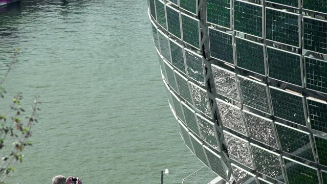 An old tourist couple photographing the solar panel design on the Seine Musicale in Paris, France