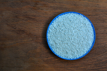Pellets of ammonium nitrate on wooden table, flat lay. Mineral fertilizer