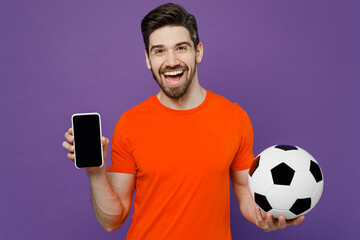 Young fan man he wear orange t-shirt cheer up support football sport team hold soccer ball watch tv...