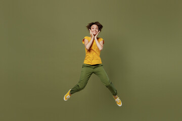 Fototapeta na wymiar Full body young shocked surprised amazed jubilant happy woman she 20s wear yellow t-shirt jump high hold face isolated on plain olive green khaki background studio portrait. People lifestyle concept.