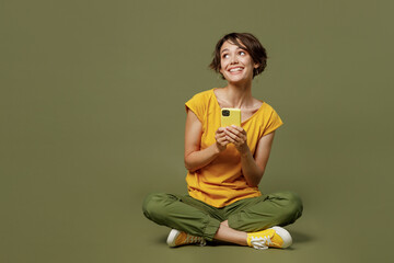 Full body young happy woman she 20s wear yellow t-shirt hold in hand use mobile cell phone browsing...