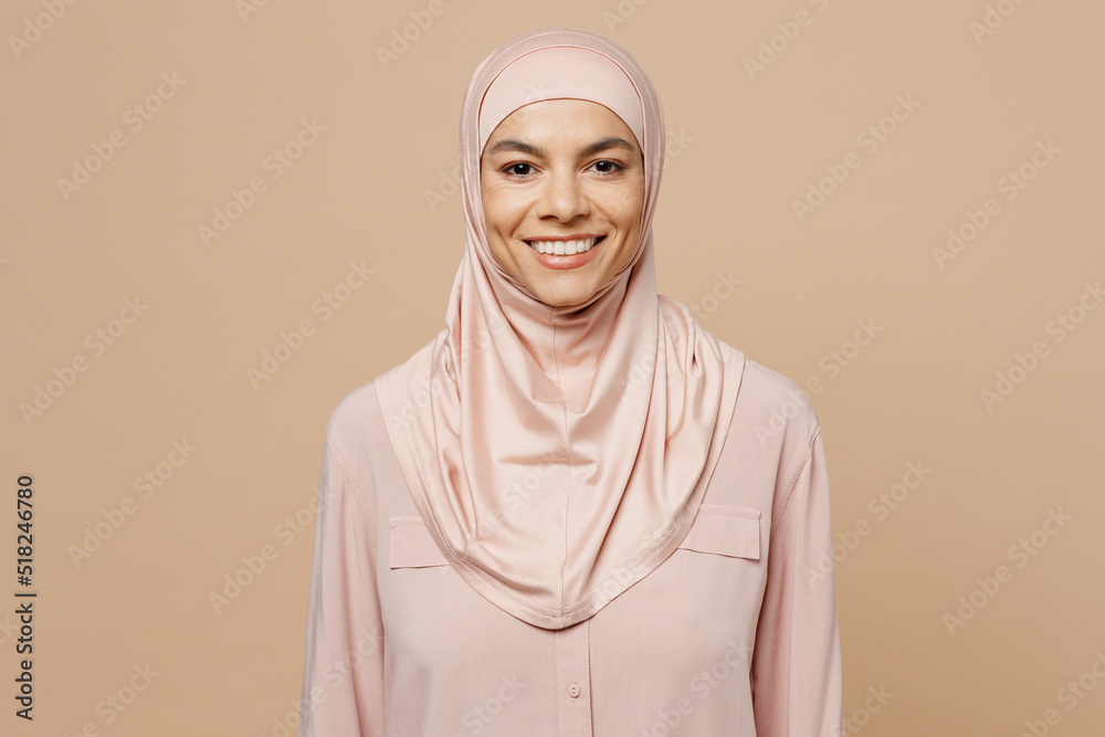 Wall mural Young fun smiling arabian asian muslim woman she 30s wear abaya hijab pink clothes look camera isolated on plain pastel light beige background studio People uae middle eastern islam religious concept