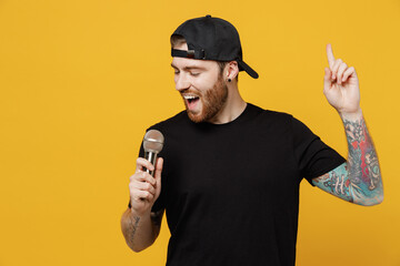 Young singer bearded tattooed man 20s he wears casual black t-shirt cap sing song in microphone at...