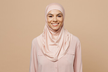 Young fun smiling arabian asian muslim woman she 30s wear abaya hijab pink clothes look camera isolated on plain pastel light beige background studio People uae middle eastern islam religious concept - obrazy, fototapety, plakaty