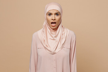 Young sad arabian asian muslim woman she wear abaya hijab pink clothes look camera with opened mouth isolated on plain pastel light beige background People uae middle eastern islam religious concept