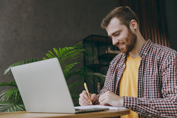 Young man he wear shirt work or study on laptop pc computer writing sit alone at table in coffee shop cafe relax rest in restaurant during free time indoors Freelance mobile office business concept.