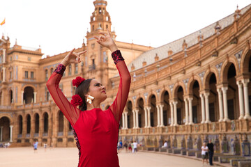 Beautiful teenage woman dancing flamenco in a square in Seville, Spain. She wears a red dress with ruffles and dances flamenco with a lot of art. Flamenco cultural heritage of humanity. - obrazy, fototapety, plakaty