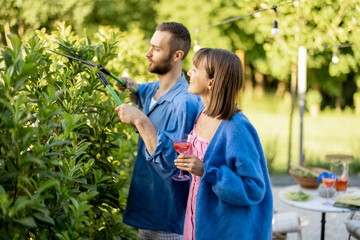 Lovely couple spend summer time at backyard of their country house on nature. Man pruning green...