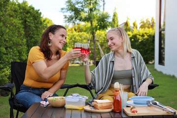 Group of happy family or friends with different ages making barbecue and celebrate outdoors with glass of red wine, grilling corn and enjoying BBQ party in backyard garden at home in summer day