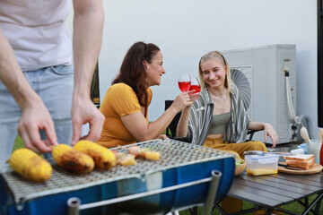 Group of happy family or friends with different ages making barbecue and celebrate outdoors with glass of red wine, grilling corn and enjoying BBQ party in backyard garden at home in summer day